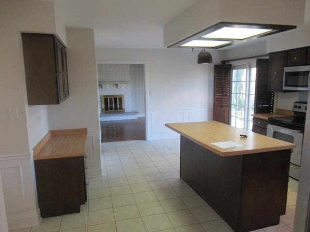 kitchen with electric stove, a center island, dark brown cabinets, and a brick fireplace