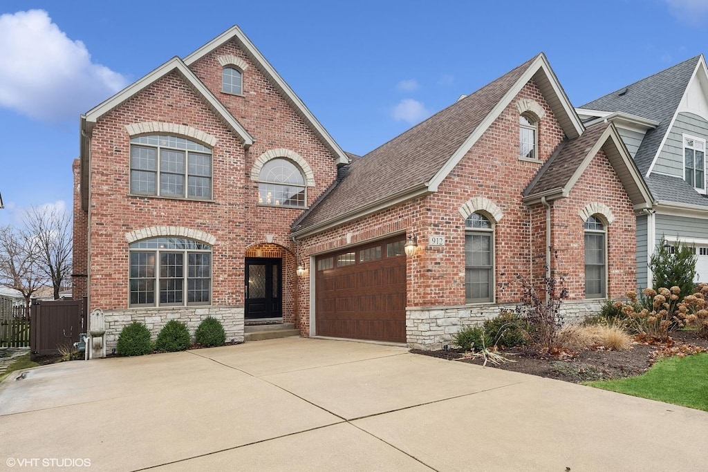 traditional-style house featuring stone siding, roof with shingles, concrete driveway, and brick siding