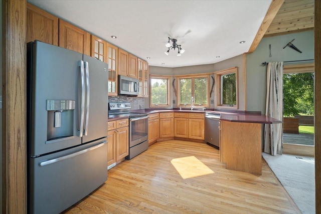 kitchen with light wood finished floors, tasteful backsplash, dark countertops, glass insert cabinets, and stainless steel appliances