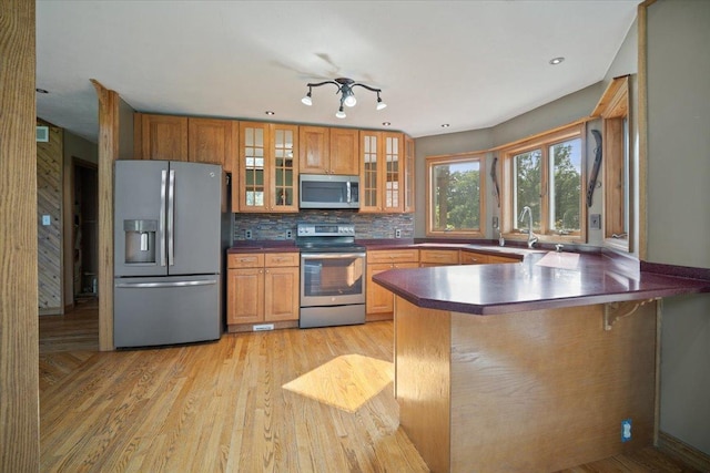 kitchen with a peninsula, a sink, appliances with stainless steel finishes, decorative backsplash, and light wood finished floors