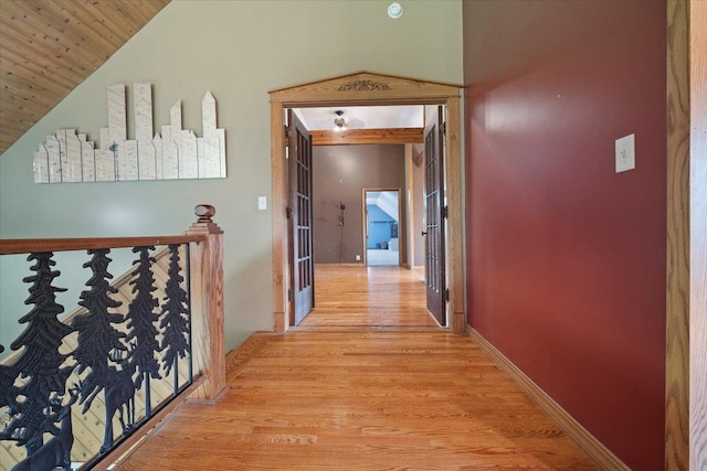 corridor featuring high vaulted ceiling, wood finished floors, an upstairs landing, and baseboards