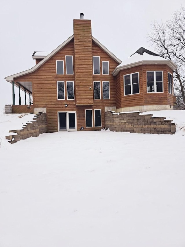 snow covered house featuring stairway and a chimney