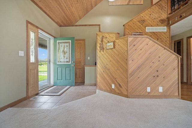 carpeted entryway featuring visible vents, wooden walls, high vaulted ceiling, and tile patterned flooring