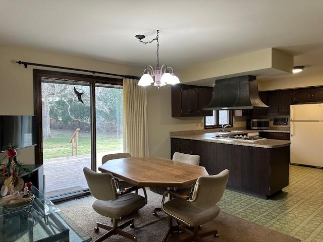 kitchen with appliances with stainless steel finishes, dark brown cabinetry, a chandelier, hanging light fixtures, and range hood