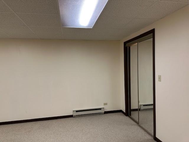 empty room with light carpet, a drop ceiling, and baseboard heating