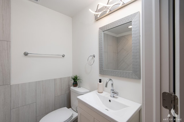 bathroom with vanity, toilet, and tile walls