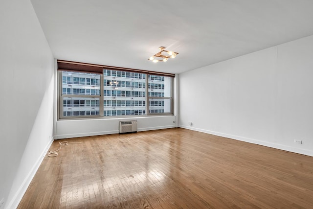 spare room with a wall mounted AC, light hardwood / wood-style floors, and an inviting chandelier