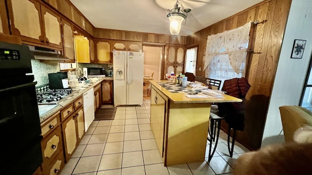 kitchen featuring stainless steel appliances, a kitchen breakfast bar, tile countertops, wooden walls, and light tile patterned floors