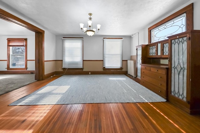 unfurnished dining area with dark hardwood / wood-style flooring, a notable chandelier, and a textured ceiling