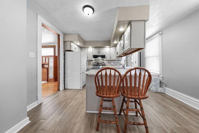 kitchen featuring electric stove, a textured ceiling, a kitchen bar, kitchen peninsula, and white fridge