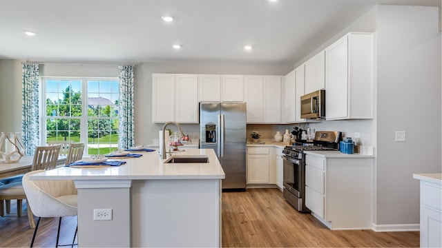 kitchen featuring a center island with sink, sink, light wood-type flooring, appliances with stainless steel finishes, and white cabinetry