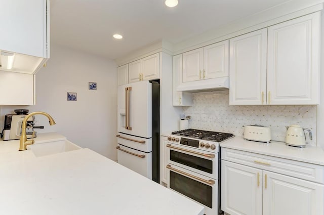 kitchen with white cabinets, high end appliances, sink, and tasteful backsplash