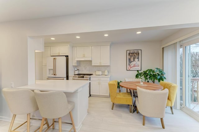 kitchen featuring backsplash, white cabinets, a kitchen breakfast bar, white fridge with ice dispenser, and gas stove