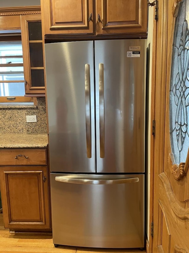 kitchen featuring light stone countertops, light hardwood / wood-style flooring, stainless steel refrigerator, and tasteful backsplash