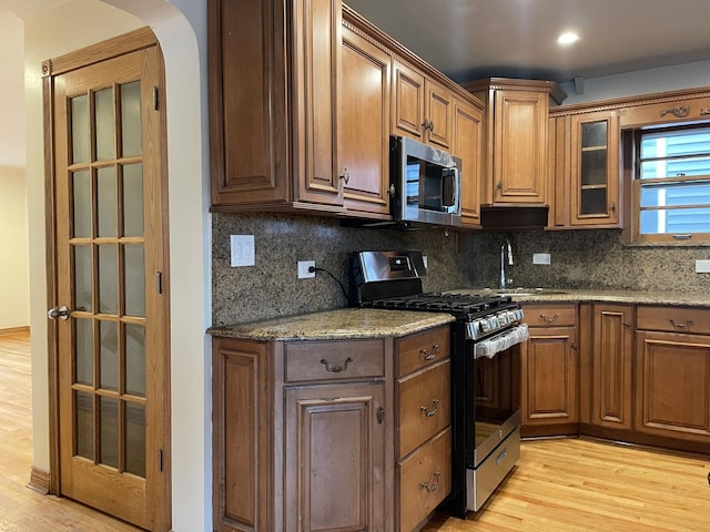 kitchen with backsplash, stainless steel appliances, light stone counters, and light hardwood / wood-style flooring