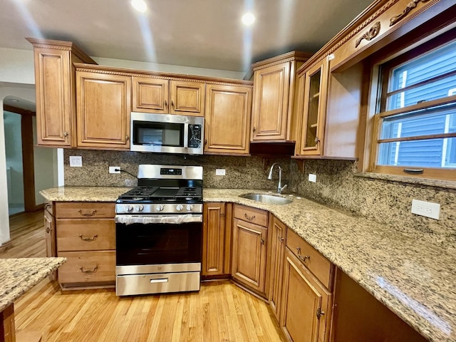 kitchen featuring light stone countertops, appliances with stainless steel finishes, decorative backsplash, sink, and light hardwood / wood-style floors