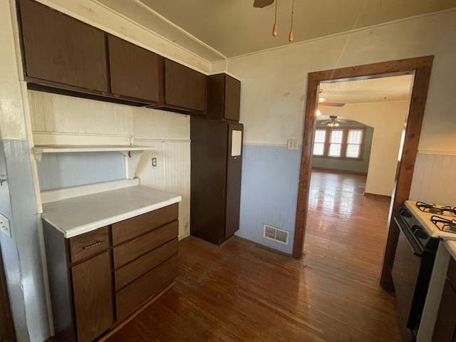 kitchen featuring ceiling fan, dark hardwood / wood-style flooring, gas range oven, and dark brown cabinets