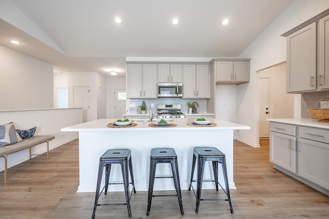 kitchen featuring a kitchen bar, lofted ceiling, gray cabinetry, range, and a kitchen island with sink