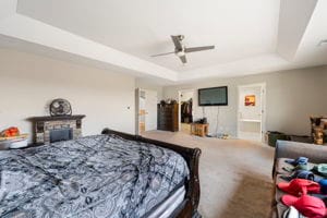 bedroom featuring carpet flooring, ceiling fan, a fireplace, and a tray ceiling