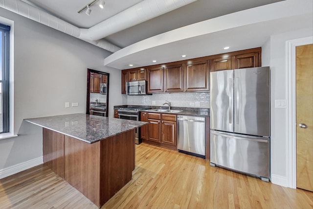 kitchen with sink, kitchen peninsula, light hardwood / wood-style floors, decorative backsplash, and appliances with stainless steel finishes