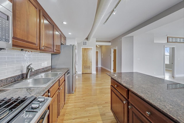 kitchen featuring sink, stainless steel appliances, light hardwood / wood-style flooring, dark stone countertops, and decorative backsplash