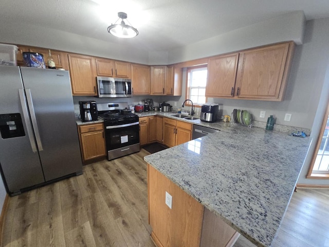 kitchen featuring light stone countertops, sink, stainless steel appliances, kitchen peninsula, and hardwood / wood-style floors