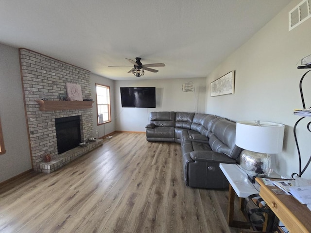 living room featuring wood-type flooring, a brick fireplace, and ceiling fan