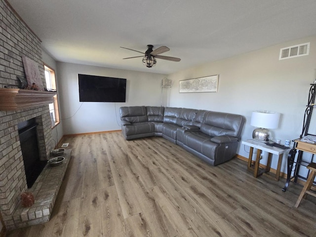 living room with ceiling fan, hardwood / wood-style floors, and a brick fireplace