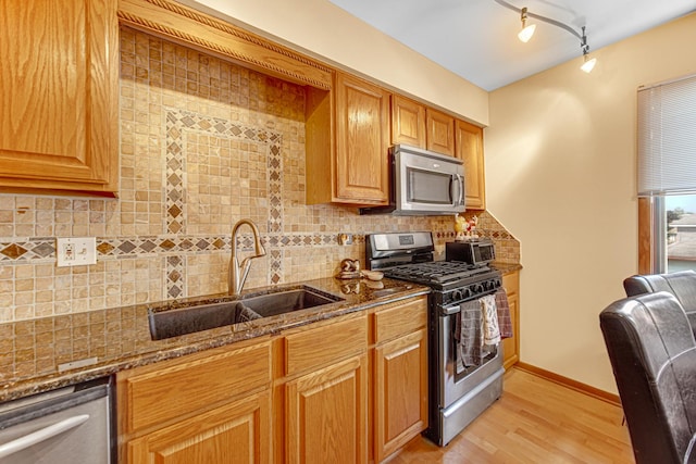 kitchen featuring sink, backsplash, dark stone countertops, appliances with stainless steel finishes, and light wood-type flooring