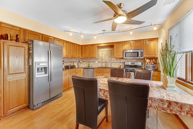 kitchen featuring appliances with stainless steel finishes, tasteful backsplash, a breakfast bar, ceiling fan, and light hardwood / wood-style floors