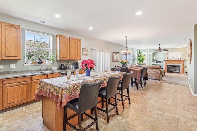 kitchen with pendant lighting, a breakfast bar, a center island, ceiling fan with notable chandelier, and sink