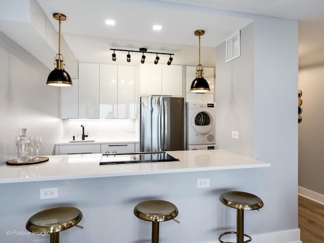 kitchen with stainless steel refrigerator, white cabinetry, kitchen peninsula, stacked washer / drying machine, and a kitchen bar