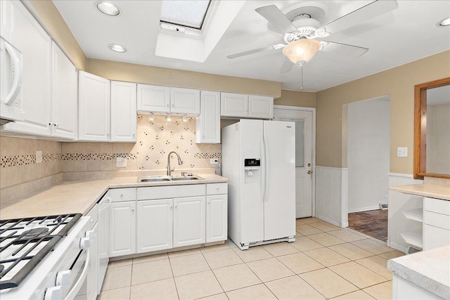 kitchen featuring a skylight, white cabinetry, sink, backsplash, and white appliances