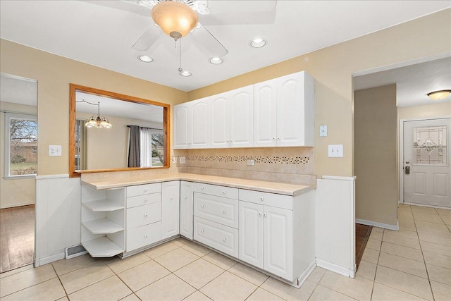 kitchen with pendant lighting, white cabinets, ceiling fan with notable chandelier, light tile patterned floors, and tasteful backsplash