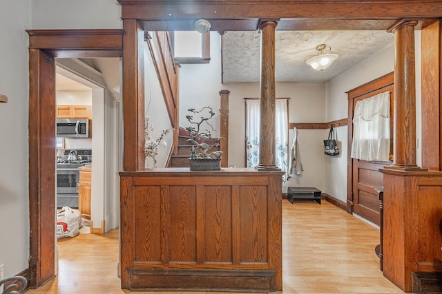 interior space with appliances with stainless steel finishes, light wood-type flooring, decorative columns, and a textured ceiling