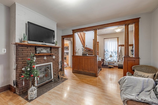 living room featuring crown molding, decorative columns, a fireplace, and light hardwood / wood-style flooring