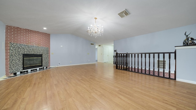 unfurnished living room with a tiled fireplace, light hardwood / wood-style floors, lofted ceiling, and a notable chandelier