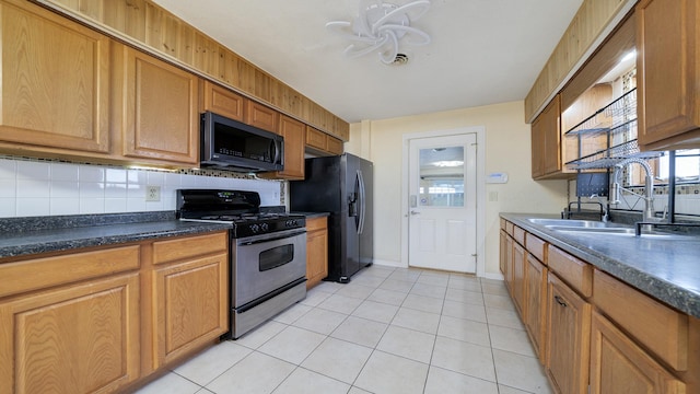 kitchen with sink, stainless steel gas range oven, backsplash, black fridge with ice dispenser, and light tile patterned floors