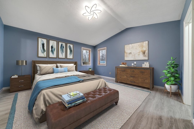 bedroom with a textured ceiling, light wood-type flooring, and vaulted ceiling