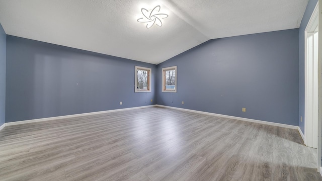 empty room featuring a textured ceiling, light hardwood / wood-style floors, and vaulted ceiling