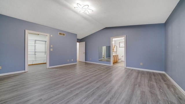 unfurnished living room with a textured ceiling, vaulted ceiling, and light wood-type flooring