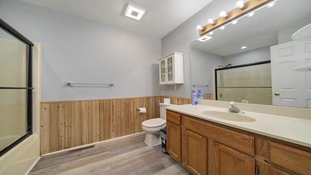 full bathroom with vanity, wooden walls, shower / bath combination with glass door, hardwood / wood-style flooring, and toilet