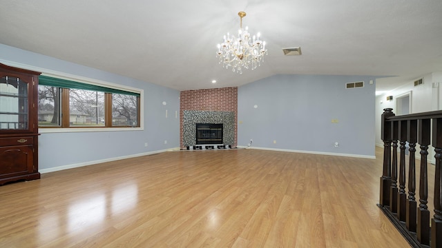 unfurnished living room with a brick fireplace, an inviting chandelier, light hardwood / wood-style floors, and vaulted ceiling