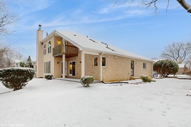 snow covered back of property featuring a balcony