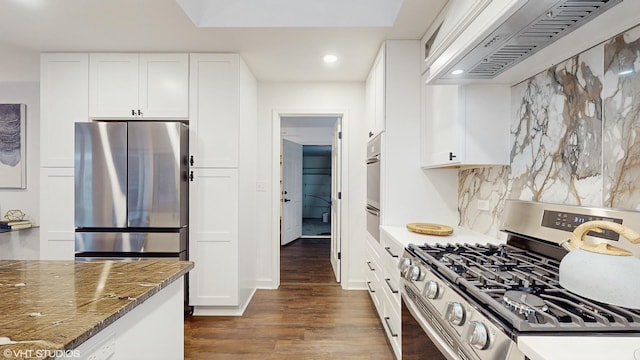 kitchen featuring decorative backsplash, appliances with stainless steel finishes, premium range hood, dark stone counters, and white cabinets