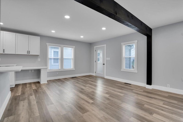 unfurnished living room featuring beam ceiling, a healthy amount of sunlight, and light wood-type flooring