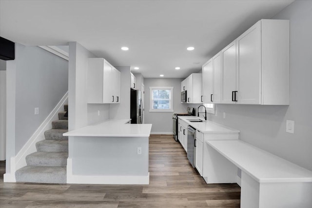 kitchen with kitchen peninsula, appliances with stainless steel finishes, light wood-type flooring, sink, and white cabinets