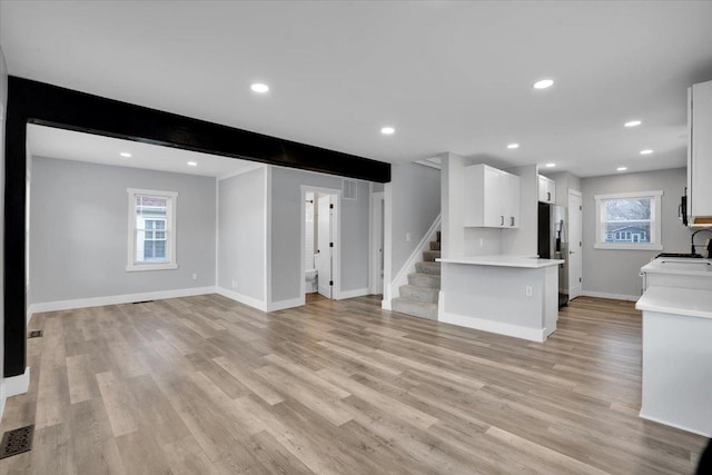 unfurnished living room with light hardwood / wood-style flooring, beamed ceiling, and sink