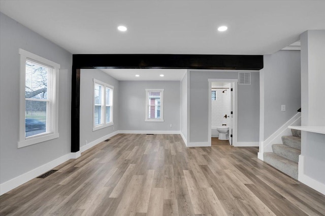 unfurnished living room featuring beam ceiling, light hardwood / wood-style flooring, and a healthy amount of sunlight