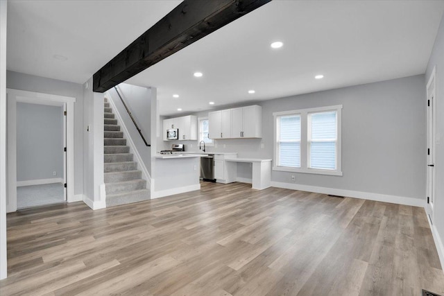 unfurnished living room with beam ceiling, sink, and light wood-type flooring